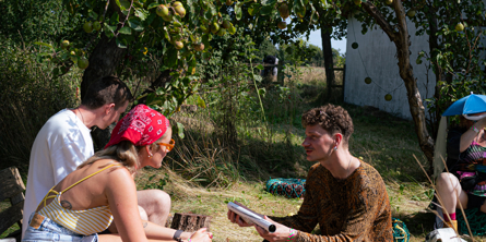 Instruktøren i workshoppen instruerer deltagerene. De sidder under et træ i sommersolen.